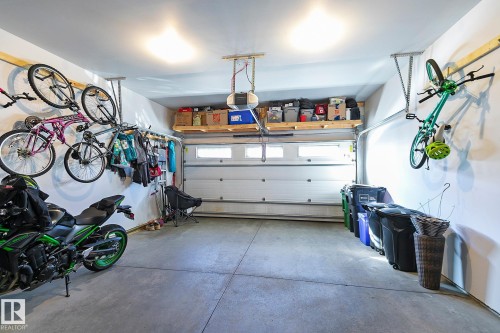 The garage features a concrete floor, a white garage door with windows, and overhead storage shelving - 17 3103 Hilton Drive, Edmonton, AB - Indoor Photo Showing Garage
