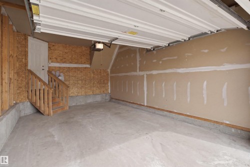 Spacious garage featuring a concrete floor, an overhead garage door mechanism, and a side entry door with a wooden staircase - 3533 11 Street, Edmonton, AB - Indoor Photo Showing Garage