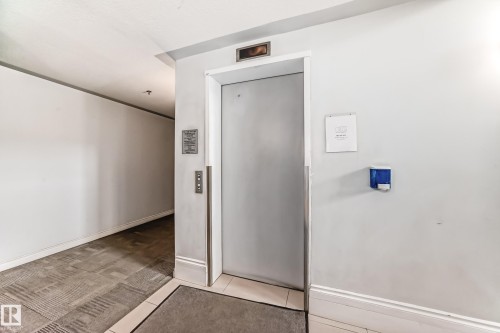 Elevator entrance featuring a metal door, call buttons, and an overhead floor indicator - 108 12028 103 Avenue, Edmonton, AB - Indoor Photo Showing Other Room