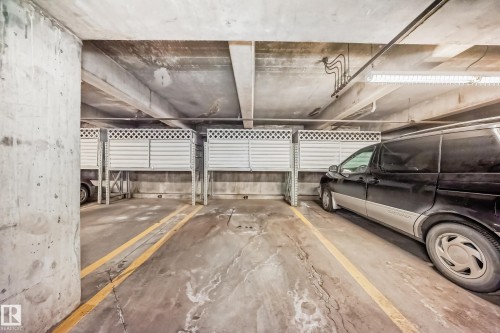Dedicated parking space within a concrete garage structure, featuring overhead lighting and adjacent storage enclosures - 108 12028 103 Avenue, Edmonton, AB - Indoor Photo Showing Garage