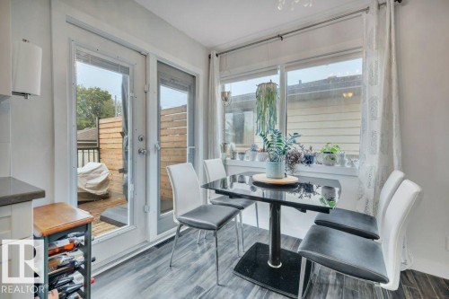 Dining area featuring wood-finish flooring, a large window with deep sill, and dual glass-paneled doors opening to a private deck with wood fencing - 7715 73 Avenue, Edmonton, AB - Indoor