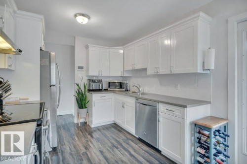 Kitchen featuring white shaker-style cabinetry, stainless steel appliances, wood-finish flooring, a white subway tile backsplash, and a contemporary flush-mount ceiling light - 7715 73 Avenue, Edmonton, AB - Indoor Photo Showing Kitchen