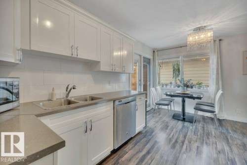 Kitchen featuring white cabinetry, a double basin sink, stainless steel dishwasher, light-toned countertops, and wood-finish flooring - 7715 73 Avenue, Edmonton, AB - Indoor Photo Showing Kitchen With Stainless Steel Kitchen With Double Sink