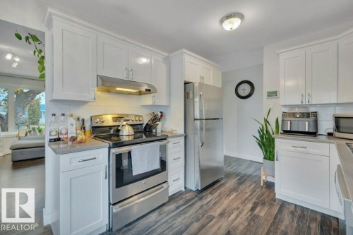 Kitchen featuring white shaker-style cabinetry, wood-finish flooring, stainless steel appliances, a tile backsplash, and light-toned countertops - 7715 73 Avenue, Edmonton, AB - Indoor Photo Showing Kitchen With Stainless Steel Kitchen With Upgraded Kitchen