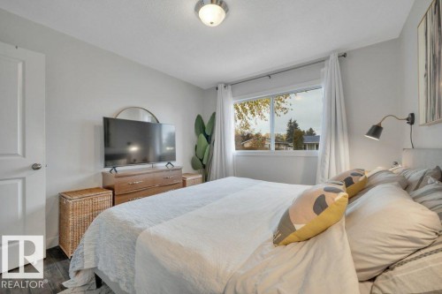 Bright room featuring a large window with white trim, wood-finish flooring, a flush-mount ceiling light fixture, and a solid white interior door - 7715 73 Avenue, Edmonton, AB - Indoor Photo Showing Bedroom