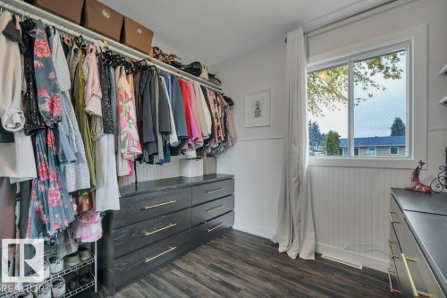 Custom closet system featuring dark wood-finish cabinetry with brass hardware, wood-finish flooring, and a window with white trim - 7715 73 Avenue, Edmonton, AB - Indoor With Storage