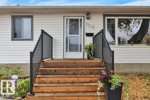 White siding exterior featuring gray trim windows, a white storm door, and wooden steps with black metal railings - 7715 73 Avenue, Edmonton, AB - Outdoor With Exterior