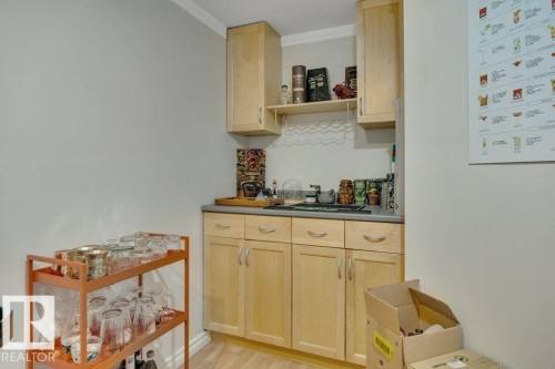 Compact kitchenette featuring light wood cabinetry, a dark countertop, an undermount sink, and upper storage with an open shelf - 7715 73 Avenue, Edmonton, AB - Indoor Photo Showing Other Room
