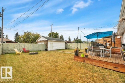 Private backyard featuring a wood deck, perimeter fencing, a detached garage with stone detailing, and a fire pit - 7715 73 Avenue, Edmonton, AB - Outdoor With Deck Patio Veranda