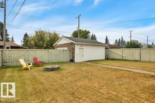 Detached garage with stone facade and vinyl siding, concrete pathway, and wooden perimeter fencing - 7715 73 Avenue, Edmonton, AB - Outdoor