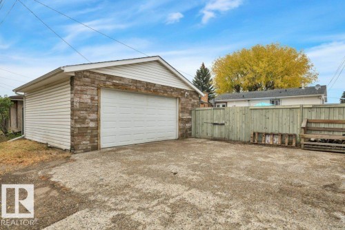 Detached garage featuring a white overhead door, horizontal siding, and stone veneer accents - 7715 73 Avenue, Edmonton, AB - Outdoor