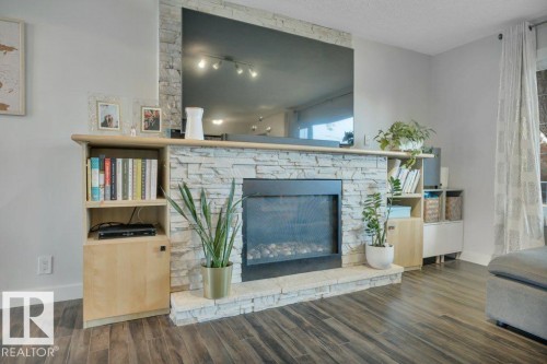 Central fireplace with stacked stone surround, a stone hearth, and built-in shelving with cabinetry - 7715 73 Avenue, Edmonton, AB - Indoor Photo Showing Living Room With Fireplace
