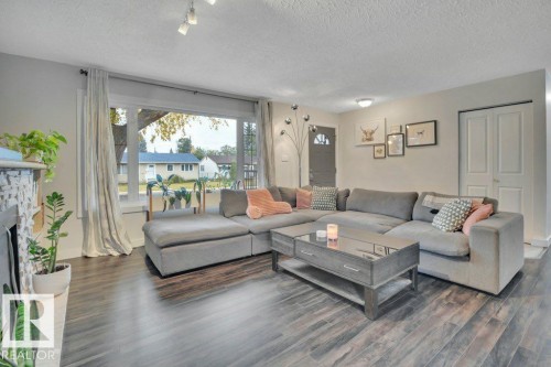 Spacious living area featuring wood-finish flooring, a large picture window, a fireplace with a tiled surround, a neutral color palette, and a white bi-fold closet door - 7715 73 Avenue, Edmonton, AB - Indoor Photo Showing Living Room