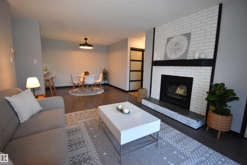 Open concept living space featuring a white brick fireplace with a dark mantle, dark wood-finish flooring, and light gray painted walls - 202 24 Alpine Place, St. Albert, AB - Indoor Photo Showing Living Room With Fireplace