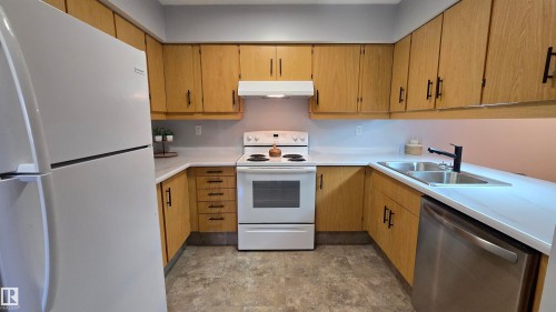 U-shaped kitchen featuring light wood-finish cabinetry with black hardware, white countertops, and a white electric range - 202 24 Alpine Place, St. Albert, AB - Indoor Photo Showing Kitchen With Double Sink
