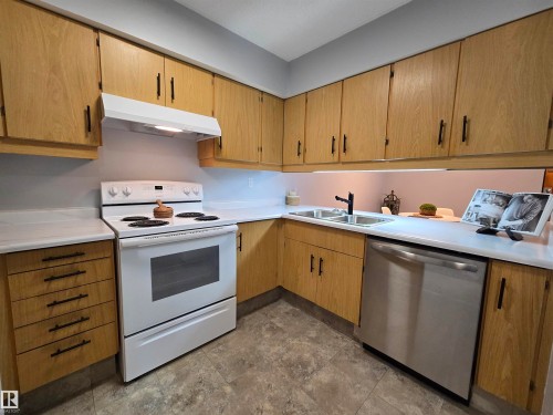 Kitchen featuring light wood cabinetry with dark hardware, a white range with a matching range hood, and a stainless steel dishwasher - 202 24 Alpine Place, St. Albert, AB - Indoor Photo Showing Kitchen With Double Sink