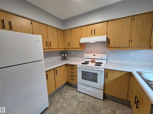 Kitchen featuring wood-finish cabinetry with dark hardware, white countertops, and a white freestanding range with overhead ventilation - 202 24 Alpine Place, St. Albert, AB - Indoor Photo Showing Kitchen
