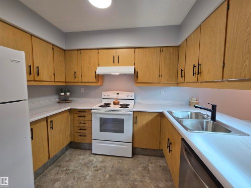 Kitchen featuring wood-finish cabinetry with black hardware, white countertops, a double basin stainless steel sink with a black faucet, and gray flooring - 202 24 Alpine Place, St. Albert, AB - Indoor Photo Showing Kitchen With Double Sink