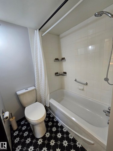 Bathroom featuring a white bathtub with a shower combination, white subway tile surround, a white toilet, and black and white patterned floor tile - 202 24 Alpine Place, St. Albert, AB - Indoor Photo Showing Bathroom