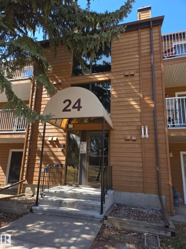 Building entrance featuring a cream-colored awning with building number, glass double doors, a concrete stoop, and black metal handrails - 202 24 Alpine Place, St. Albert, AB - Outdoor