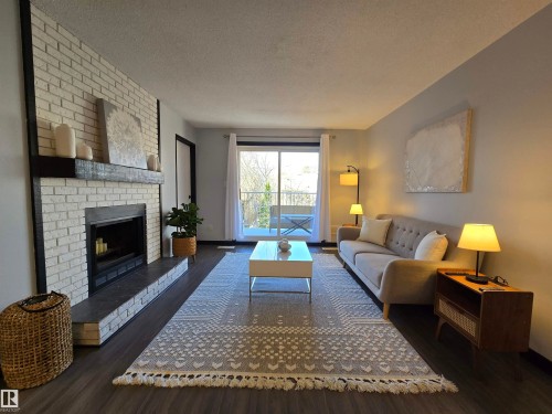 Living area featuring a painted brick fireplace with a dark mantel, dark wood-finish flooring, light-toned walls, and a sliding glass door leading to an outdoor space - 202 24 Alpine Place, St. Albert, AB - Indoor Photo Showing Living Room With Fireplace