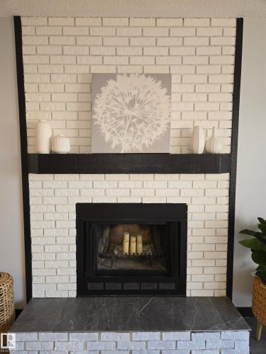 White-painted brick fireplace featuring a black mantel, dark-toned hearth tiling, and a black fireplace insert - 202 24 Alpine Place, St. Albert, AB - Indoor Photo Showing Living Room With Fireplace