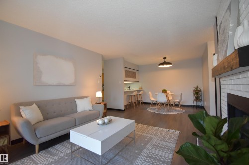 Living area featuring wood-finish flooring, a white brick fireplace with a wood mantle, and an open concept layout - 202 24 Alpine Place, St. Albert, AB - Indoor Photo Showing Living Room With Fireplace