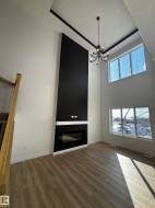 This living area features high ceilings with a striking black accent, a modern chandelier, and large windows that provide abundant natural light - 