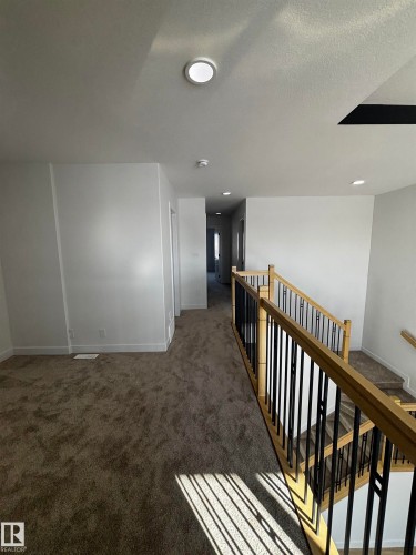 The property features a staircase with light wood railings and black vertical spindles, leading down to carpeted steps - 2012 210 St, Edmonton, AB - Indoor Photo Showing Other Room