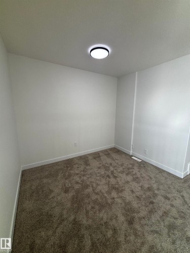 This room features plush grey carpeting, white walls, white baseboards, and a modern circular ceiling light fixture - 2012 210 St, Edmonton, AB - Indoor Photo Showing Other Room