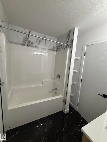 Bathroom featuring a white tub and shower combination with a modern shower head and fixture, dark marble-style tile flooring, and a white interior door with a black handle - 2012 210 St, Edmonton, AB - Indoor Photo Showing Bathroom