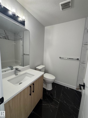 Bathroom featuring a light wood vanity with a white countertop, a rectangular mirror, and black marble-patterned floor tiles - 2012 210 St, Edmonton, AB - Indoor Photo Showing Bathroom