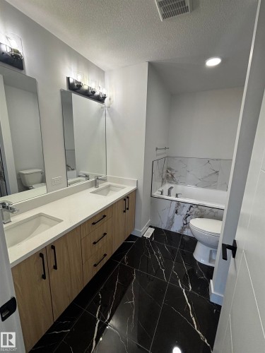 Bathroom featuring a double vanity with two sinks, black marble-style floor tiles, and a built-in bathtub with white and gray marble-style wall tiles - 2012 210 St, Edmonton, AB - Indoor Photo Showing Bathroom