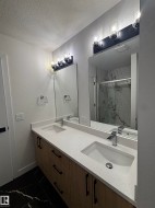 Bathroom featuring a double vanity with a light-colored countertop and wooden cabinetry, two rectangular mirrors, and black tiled flooring - 