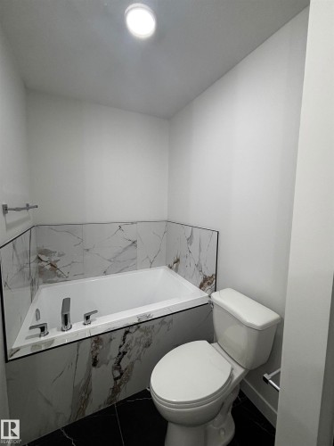 Bathroom featuring a built-in tub with chrome fixtures, a tiled surround, and black floor tiles - 2012 210 St, Edmonton, AB - Indoor Photo Showing Bathroom