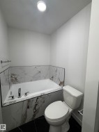 Bathroom featuring a built-in tub with chrome fixtures, a tiled surround, and black floor tiles - 