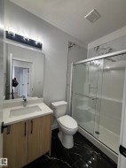 The bathroom features a vanity with a white countertop and a rectangular sink, set against a black marble-patterned floor - 