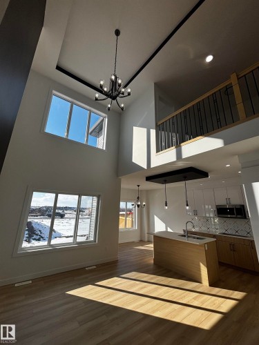 The open concept living area features high ceilings with a modern chandelier, large windows providing abundant natural light, and light-toned flooring - 2012 210 St, Edmonton, AB - Indoor Photo Showing Other Room