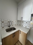 Utility area featuring a stainless steel sink, light-colored countertops, and patterned backsplash - 