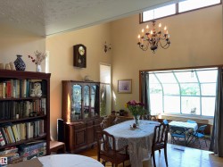 Dining area featuring vaulted ceilings, a multi-tier chandelier, high transom windows, hardwood flooring, and a sunroom extension with expansive windows - 