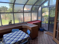 Sunroom featuring a curved glass roof, brick-patterned flooring, built-in wooden cabinetry, a built-in planter with a red countertop, and direct access to an outdoor deck - 