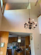 Vaulted ceiling featuring a multi-arm chandelier, an upper-level window, and an exposed ceiling fan - 