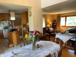 Open-concept living space featuring a kitchen with wood cabinetry and a stainless steel range hood, a dining area with wood-finish flooring, and a living area with a large window - 