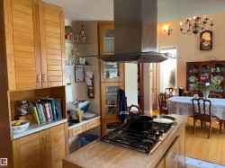 Kitchen featuring a built-in cooktop with an overhead stainless steel range hood, natural wood cabinetry, and a light-toned countertop - 