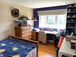 Interior room featuring wood-finish flooring, a large window with roller shades, and a built-in shelving unit - 