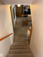 Carpeted staircase with wood handrail leading to a lower-level space featuring carpeted flooring, a ceiling-mounted light fixture, and bifold closet doors - 