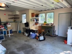Concrete floor garage featuring an exposed ceiling structure with joists, two windows with light green trim, a side door, and built-in shelving units - 