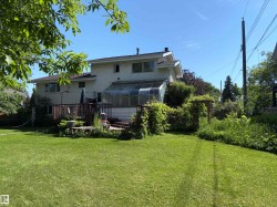 Expansive backyard featuring a manicured lawn, a multi-level wood deck, an attached sunroom, and mature perimeter landscaping - 