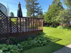 Expansive lawn area with mature trees, complemented by a wooden deck featuring lattice skirting and a privacy screen - 