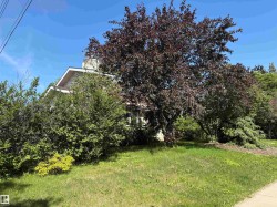 Mature trees and established shrubbery complement a partial glimpse of the property's exterior, featuring a visible roofline and gable - 